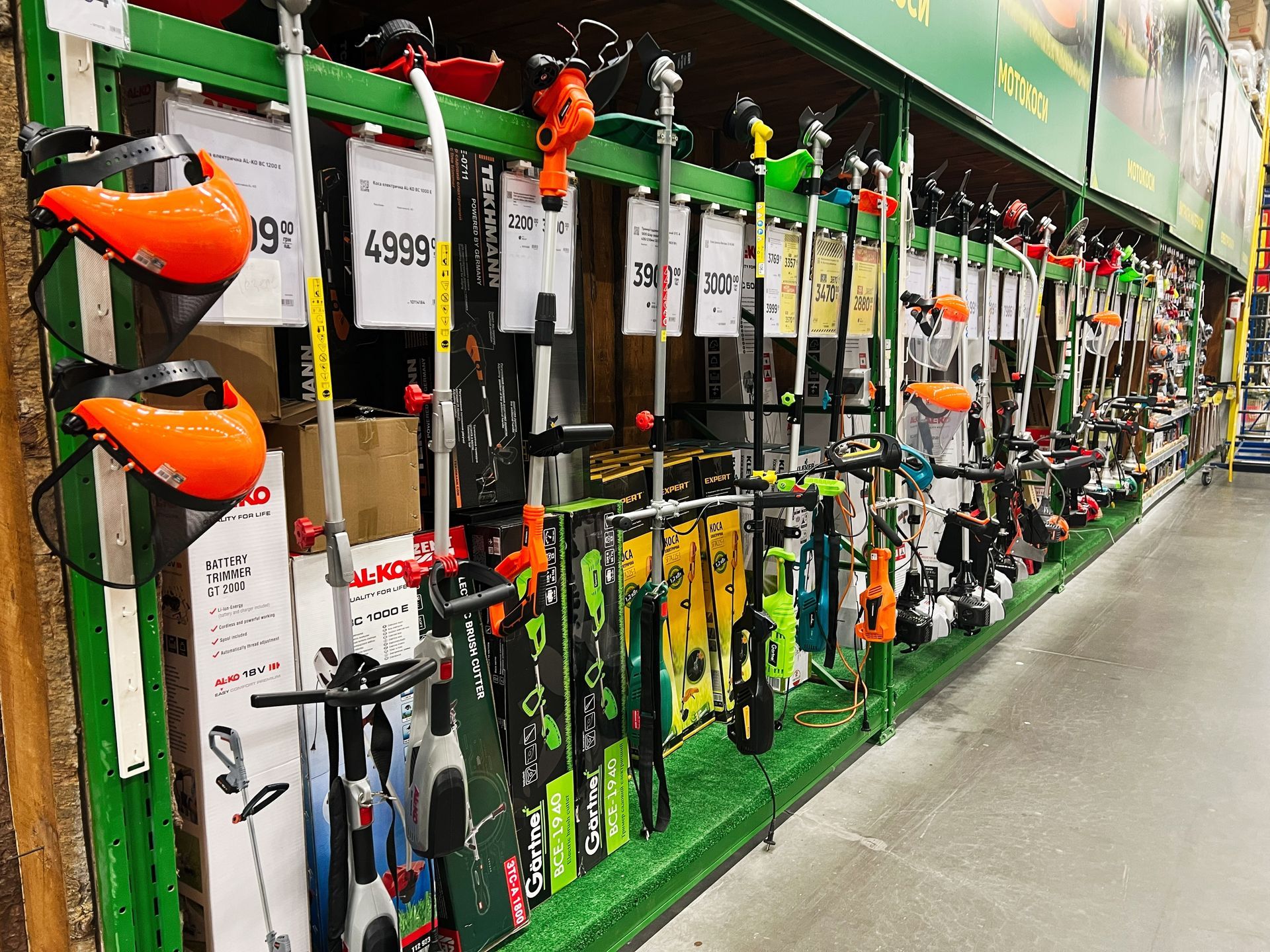 A row of lawn mowers are lined up on a shelf in a store.