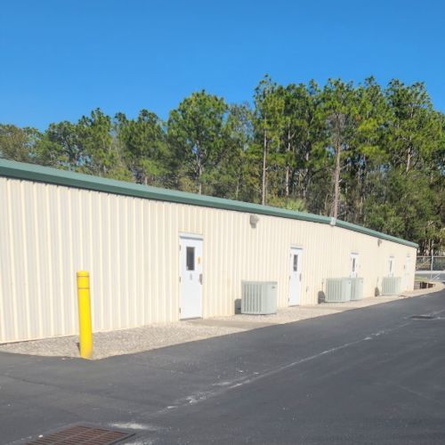 Storage units building with a white metal exterior, blue sky, and trees in the background.