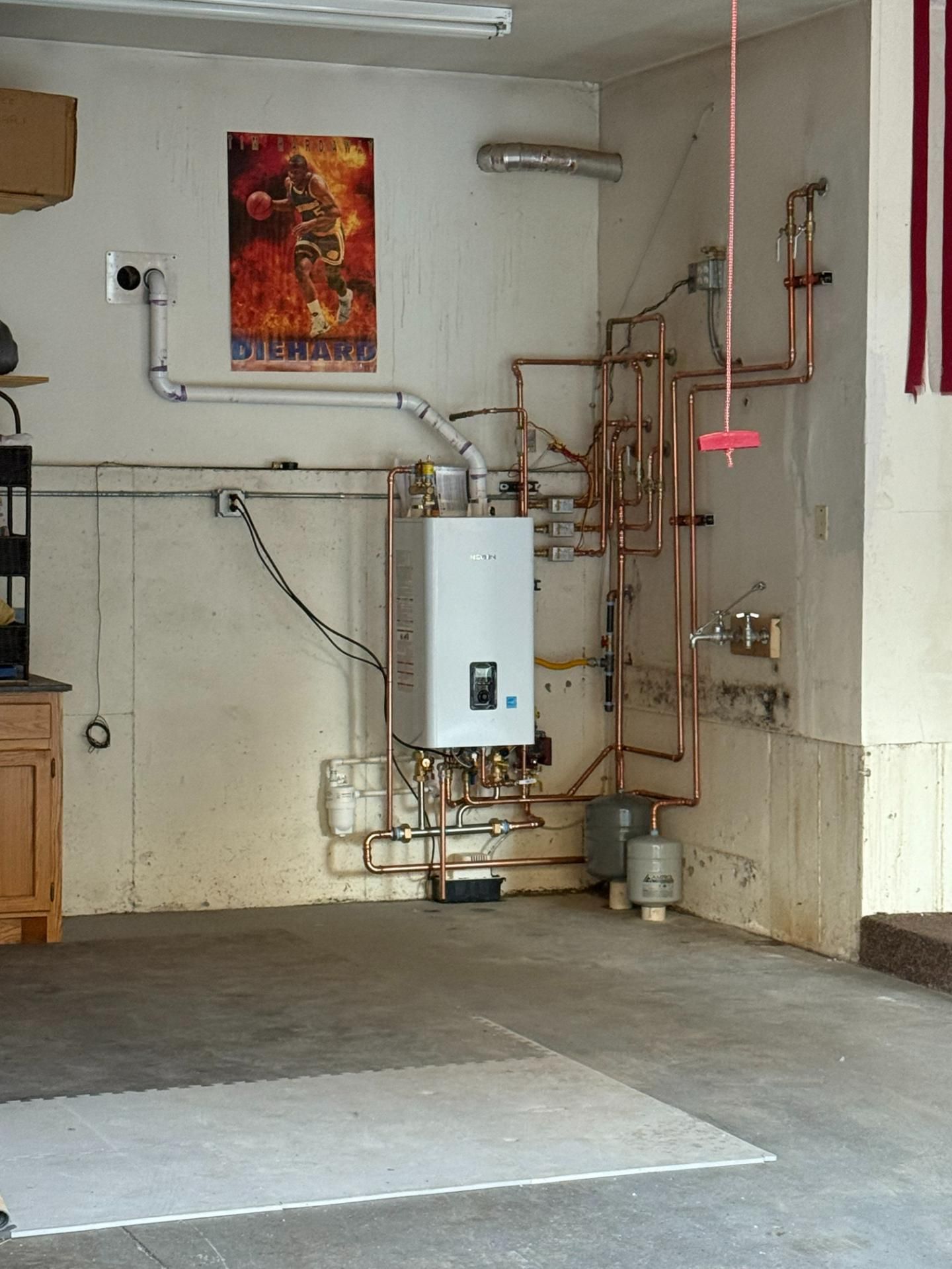 White water heater in a garage with copper pipes and a poster.