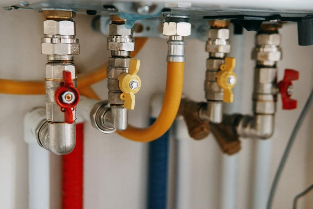 Pipes and valves, some with red and yellow handles, connected to a white surface.