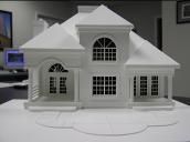 White architectural model of a house with various window shapes, porch, and a chimney.