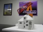 White model house on a white table with a purple and orange sign in the background.