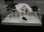 Architectural model of a white house with trees, displayed in a clear box.