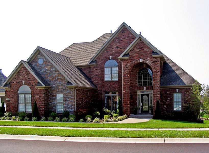 Brick house with stone accents, arched windows, and green lawn.