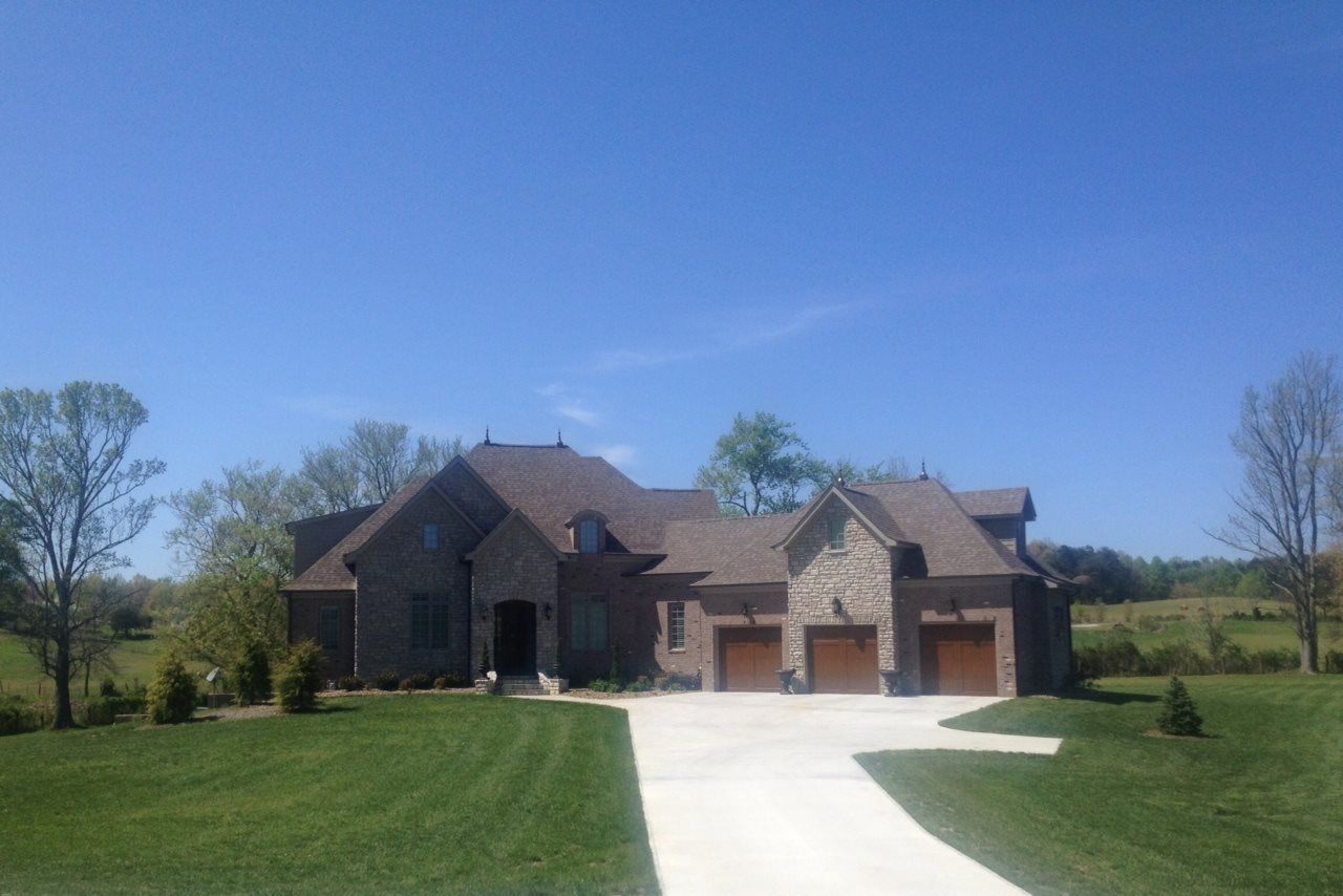Brick house with three-car garage, brown roof, and concrete driveway under a blue sky.