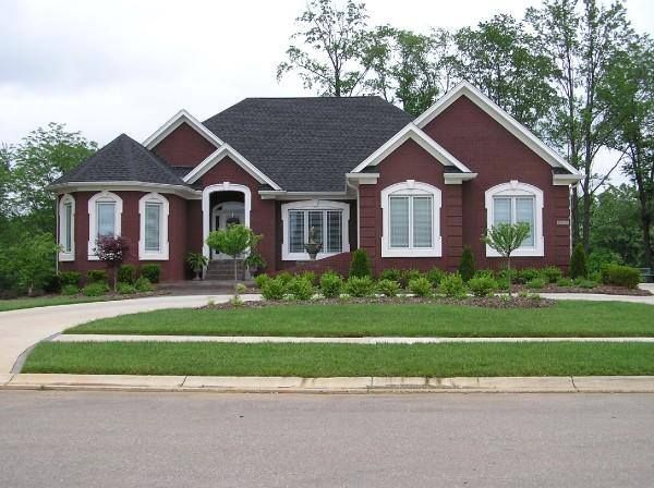 Red brick house with white trim, black roof, and green lawn. Driveway curves to the left.