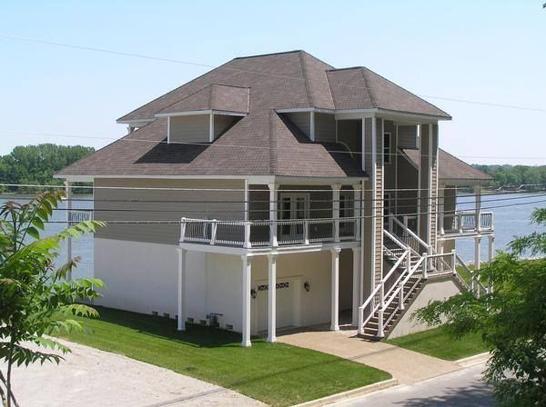 Two-story building with a brown roof and screened porches, next to a body of water.