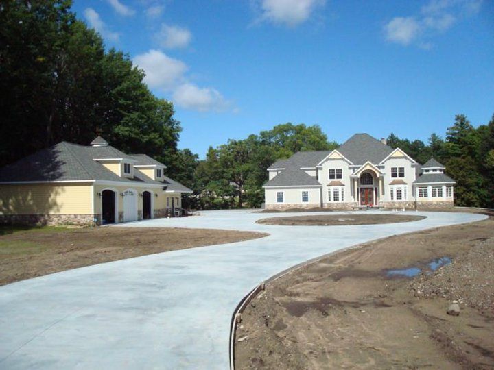 A large cream-colored house and detached garage on a concrete driveway under a blue sky.