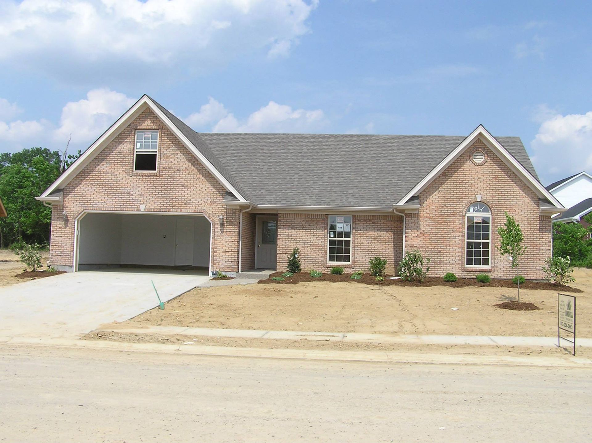 New house under construction with exposed sheathing, garage, and driveway. Blue sky.