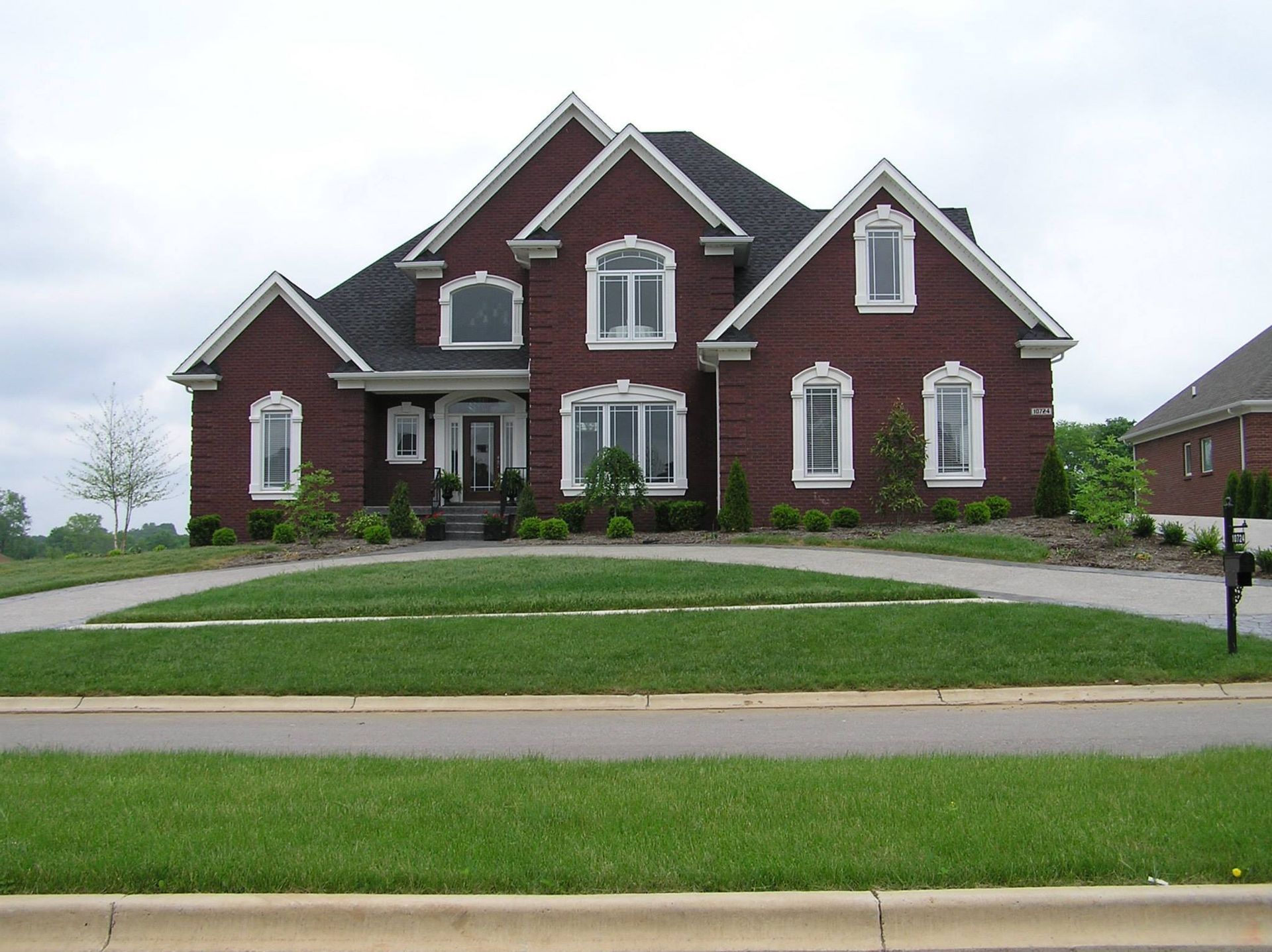 Red brick two-story house with white trim, arched windows, and a circular driveway on a grassy lawn.