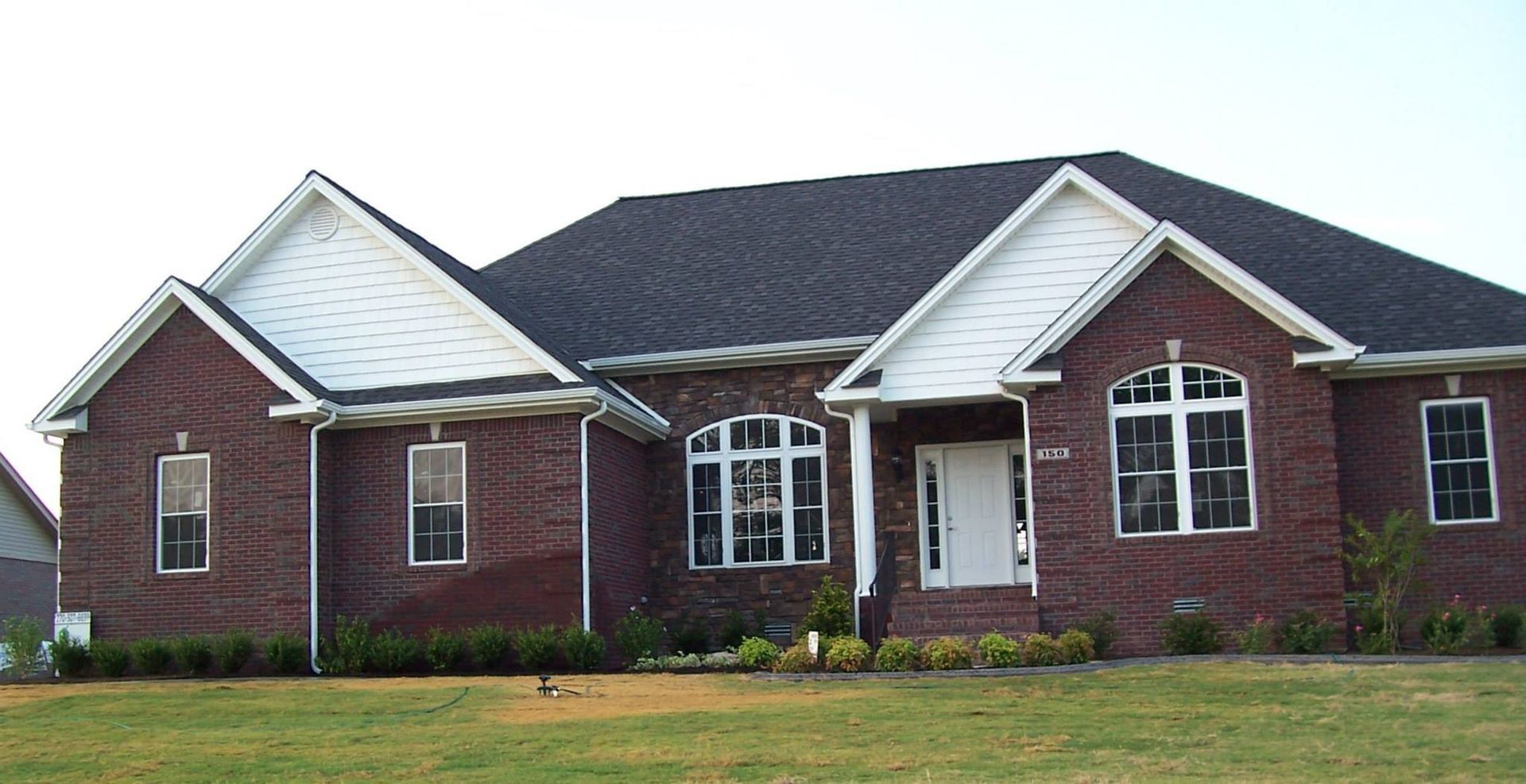 Red brick house with dark roof and white trim, set on a grassy lawn.
