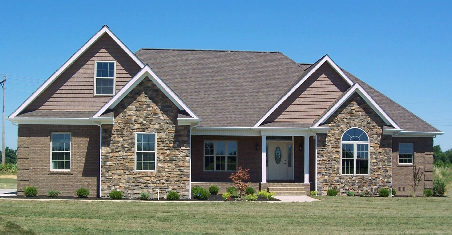 Ranch-style house with stone and brick exterior, brown roof, and blue sky.