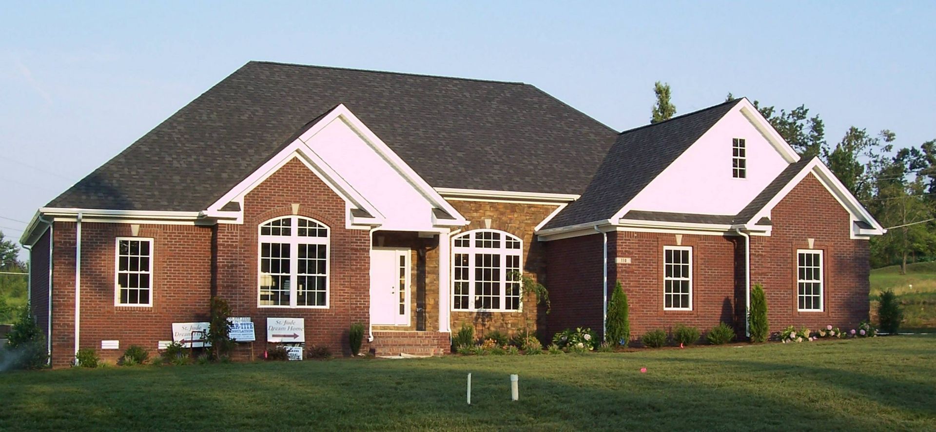 Brick house with dark roof and white trim in a grassy yard.