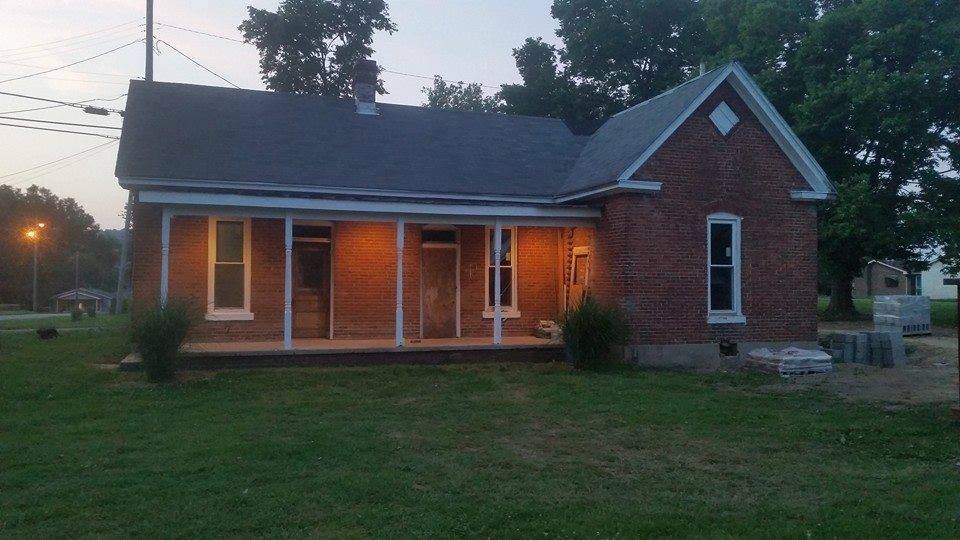 Brick house with a porch and lit windows at dusk.