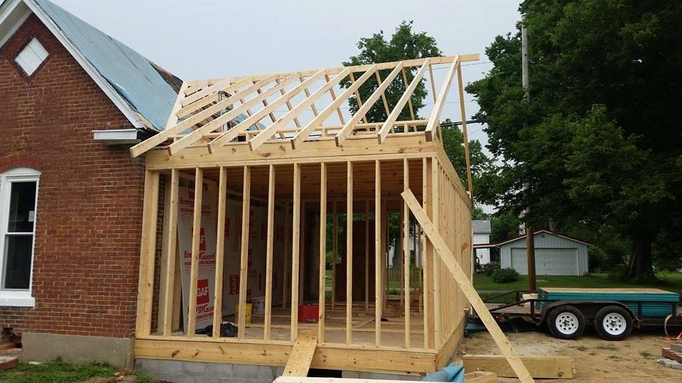 Wooden structure of a room being added to a brick house under construction, outdoor setting.