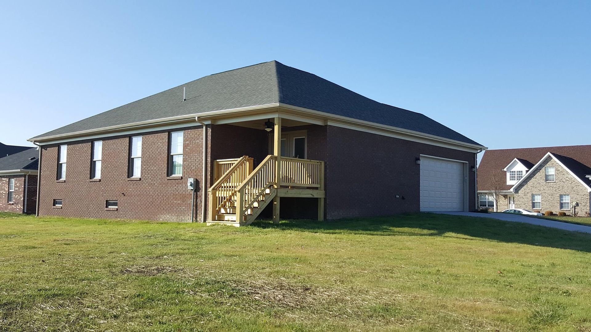 Brick house with a covered porch and wooden steps, on a grassy lawn under a clear sky.