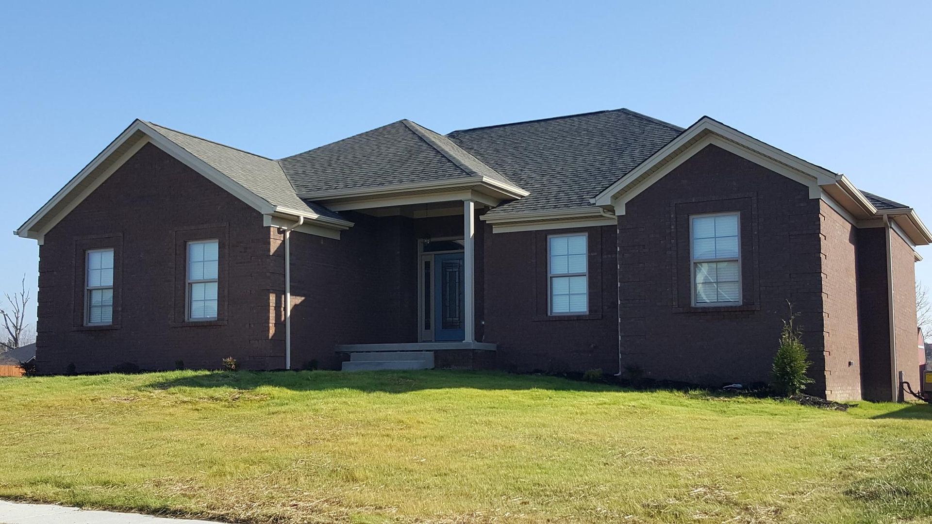 Brick house with a dark roof and green grass in front.