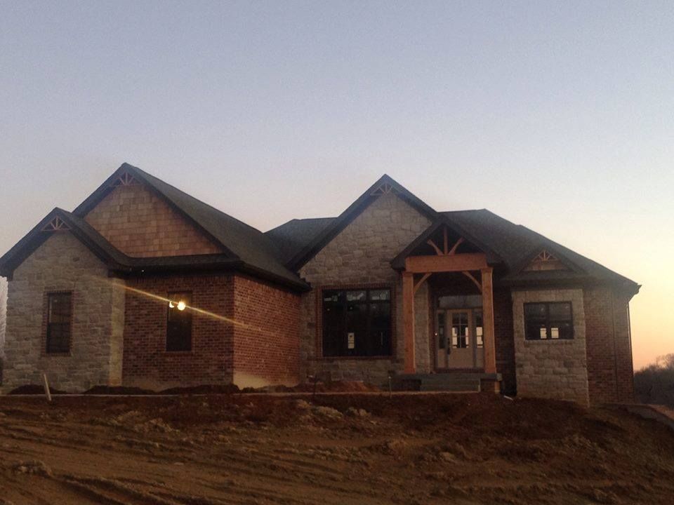 New house with brick and stone exterior under construction, dusk setting.