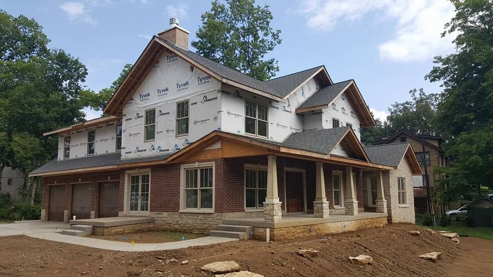 Two-story house under construction with brick facade, porch, and unfinished exterior.