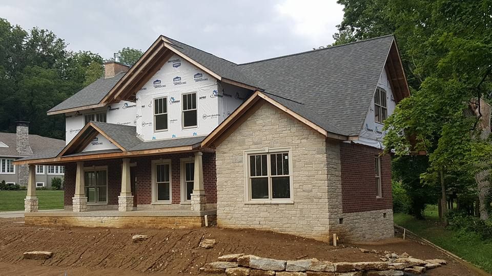 Two-story house under construction with stone, brick, and gray roofing. Construction materials are visible.