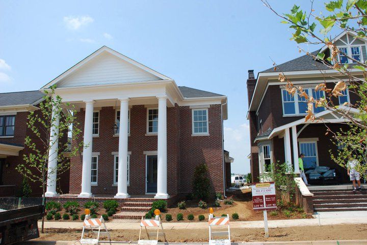 Two brick houses; one with white columns, the other with a porch and dark roof. Construction signs in foreground.