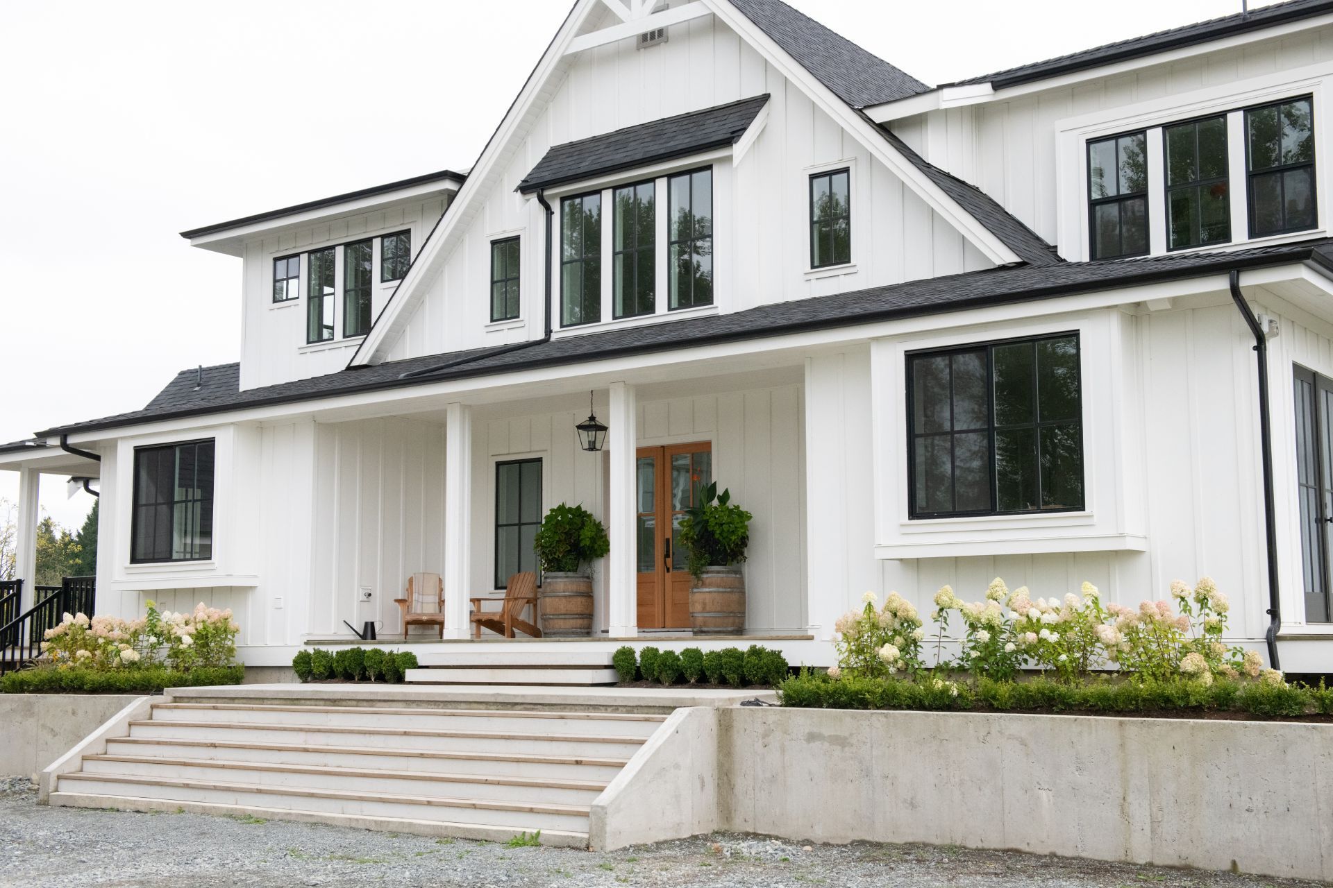White farmhouse with black windows and roof, featuring a porch, steps, and landscaping.