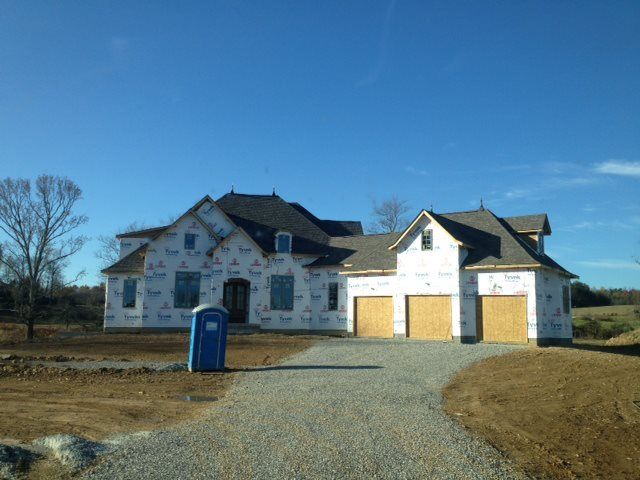 A house under construction with a gravel driveway and a blue portable toilet on a sunny day.