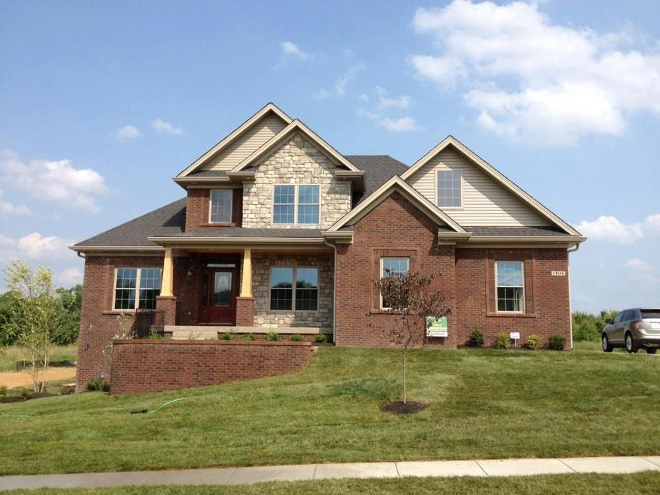 Red brick house with stone accents, on green lawn under blue sky.
