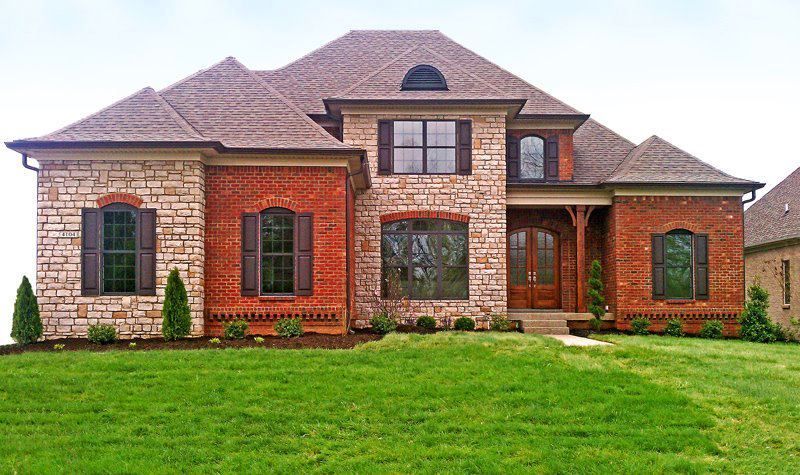 Two-story house with brick and stone facade, brown roof, and green lawn.
