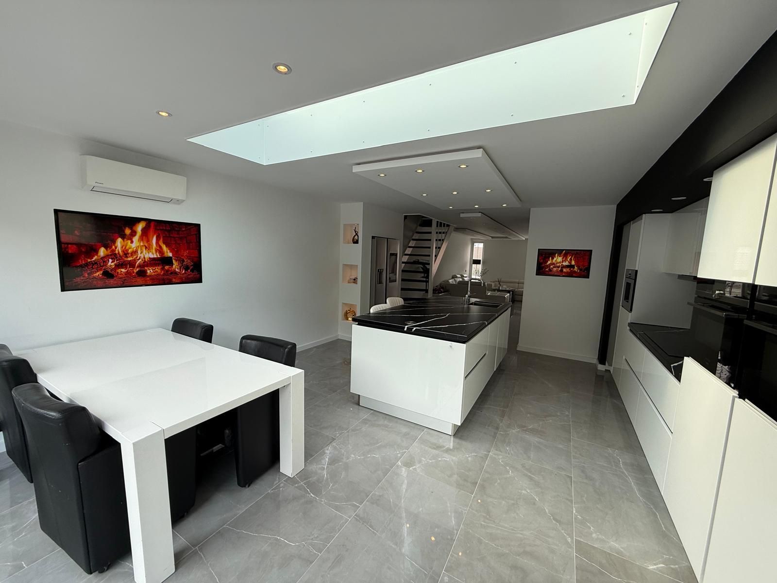 Moderne keuken met witte kasten, kookeiland, eettafel en dakraam. Grijze tegelvloer.