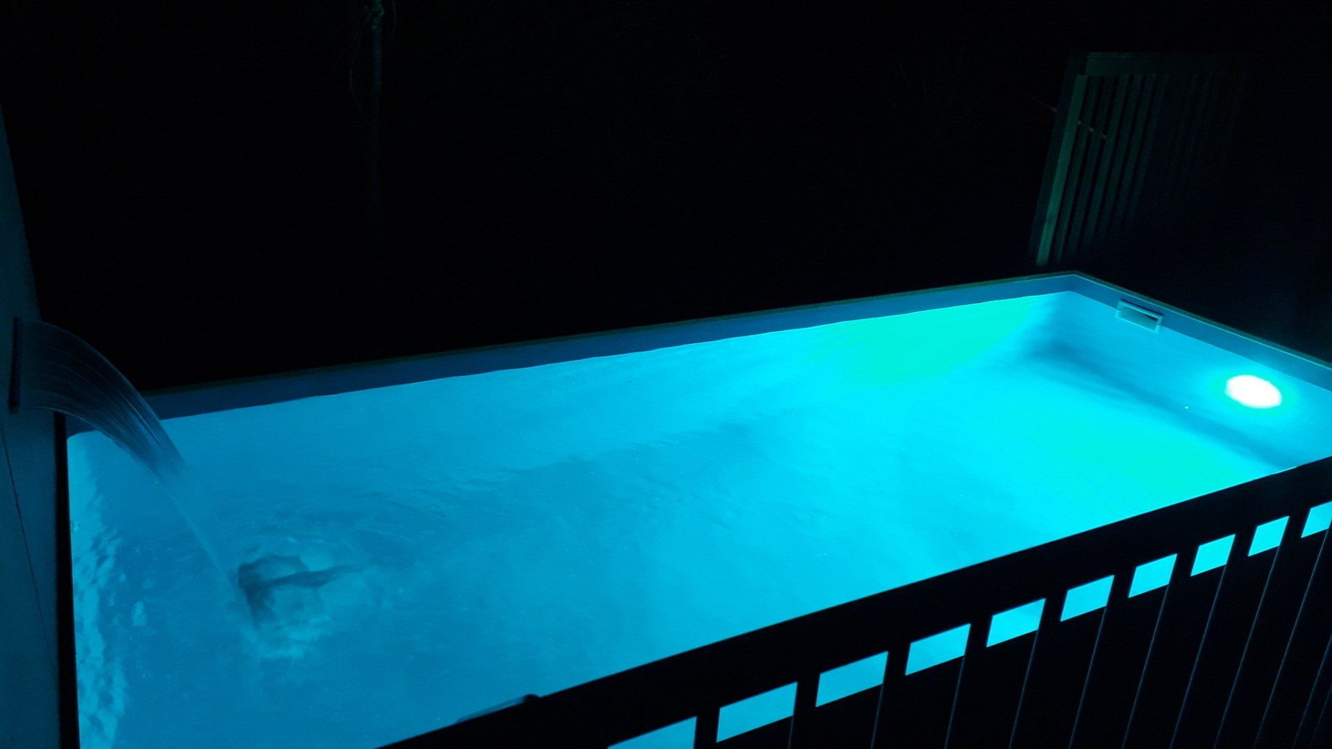 A swimming pool is lit up at night with blue lights.