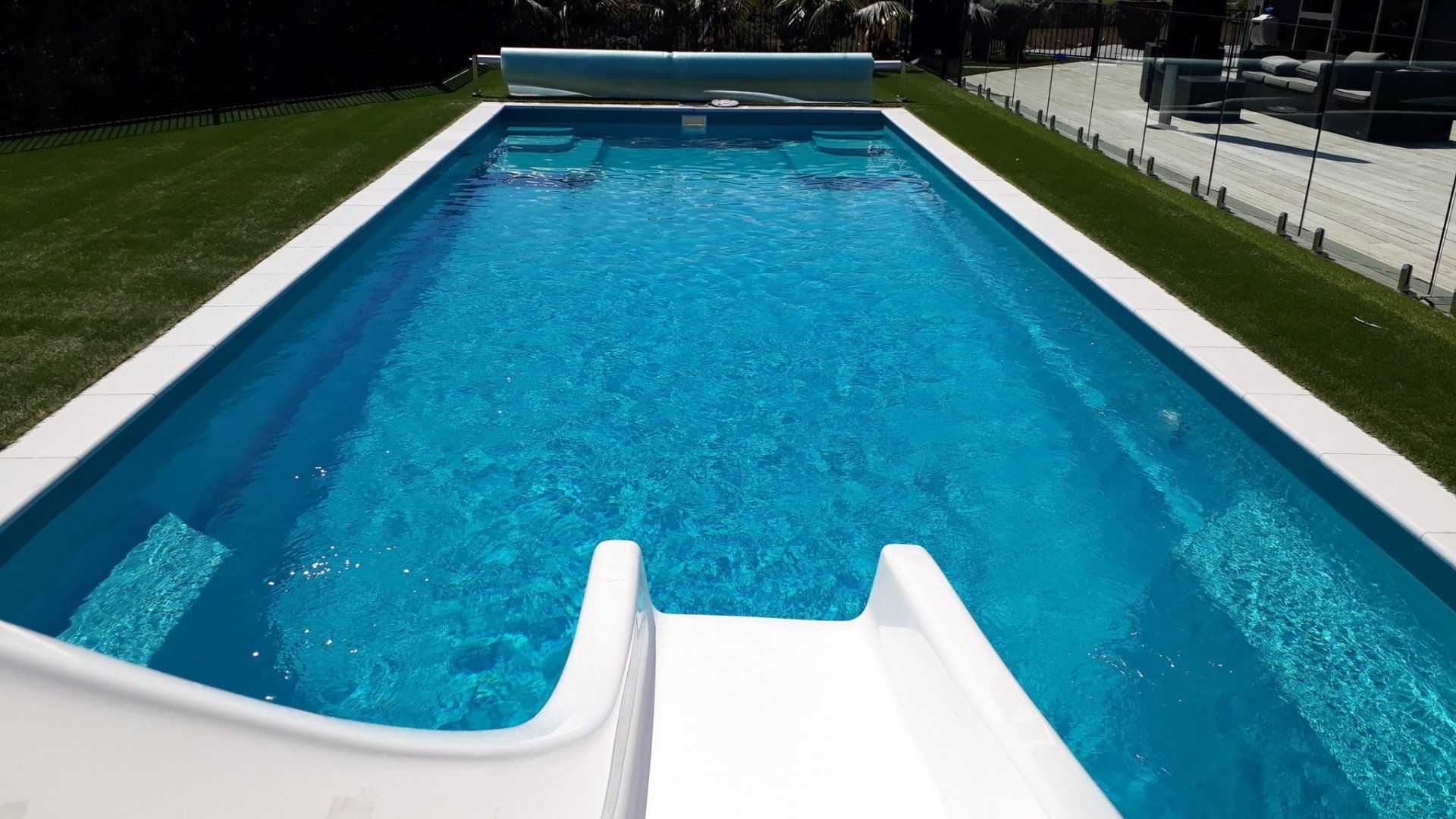 A large swimming pool with a slide in the middle of it. Poolcorp Pools Auckland