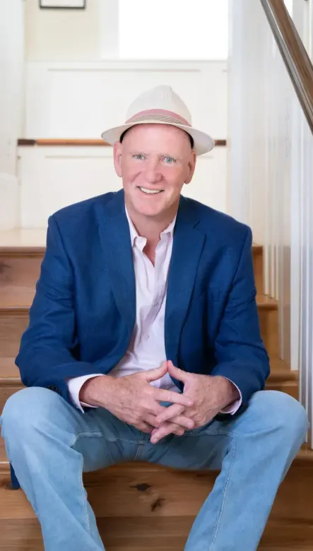 A man wearing a hat and a blue jacket is sitting on a set of stairs.