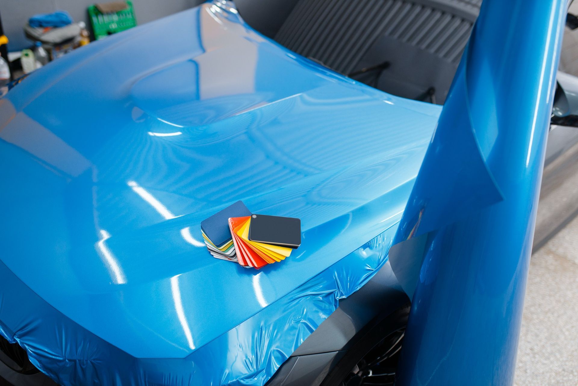 Blue car hood wrapped in protective film, with a small tool and color swatches on top