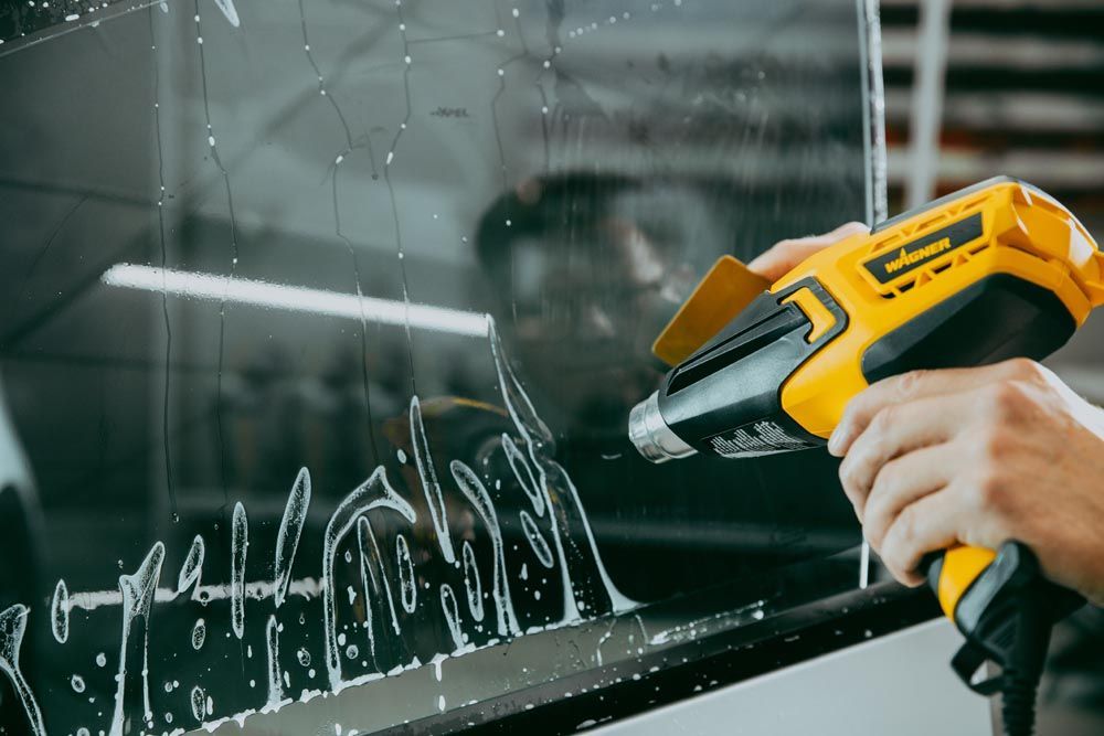 Person using a yellow heat gun to remove vinyl lettering from a car window