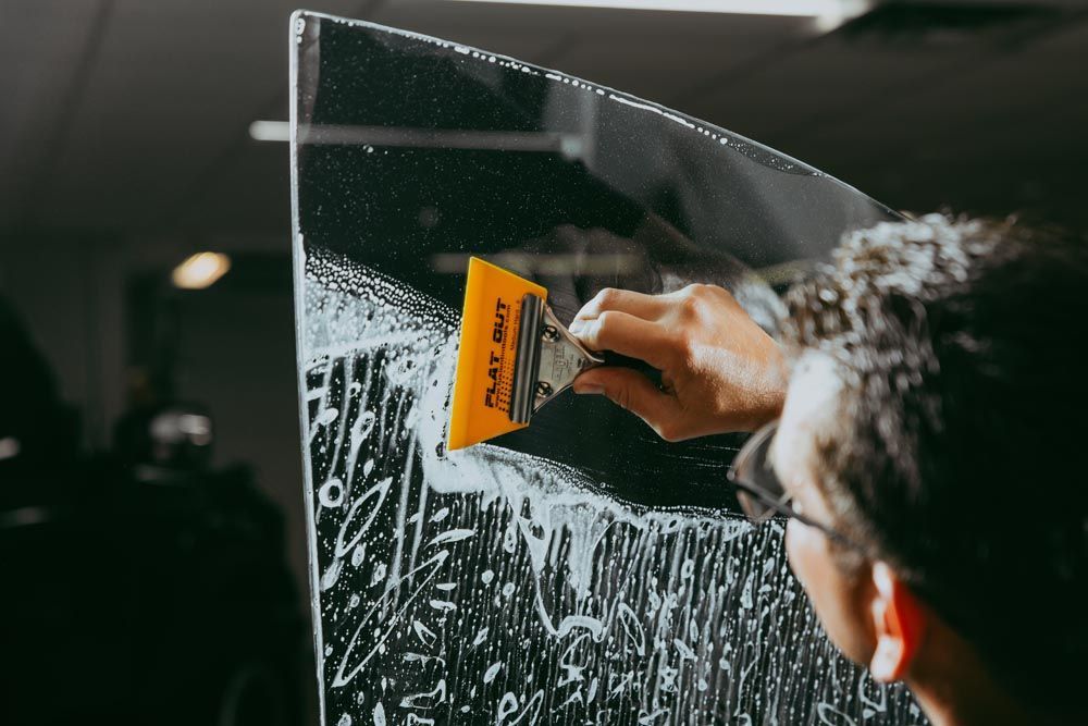 Person cleaning a glass window with a squeegee, wiping away soapy water in a workshop.