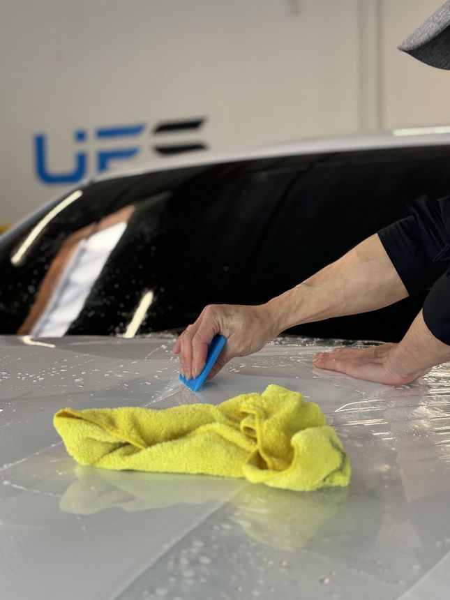 Hand polishing a car hood with a yellow cloth and blue applicator in a garage