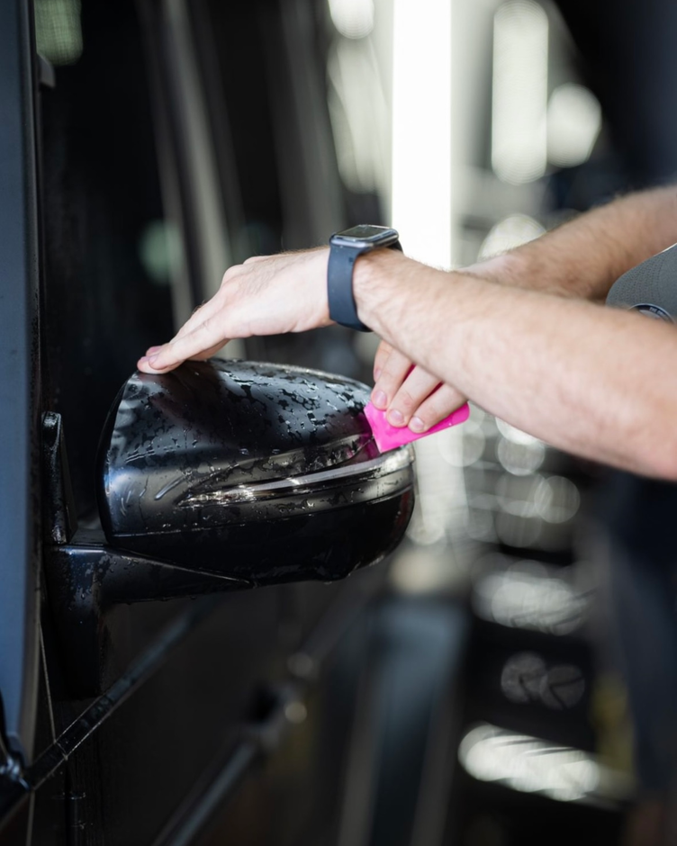 Person wiping a black car side mirror with a pink cloth at a car wash