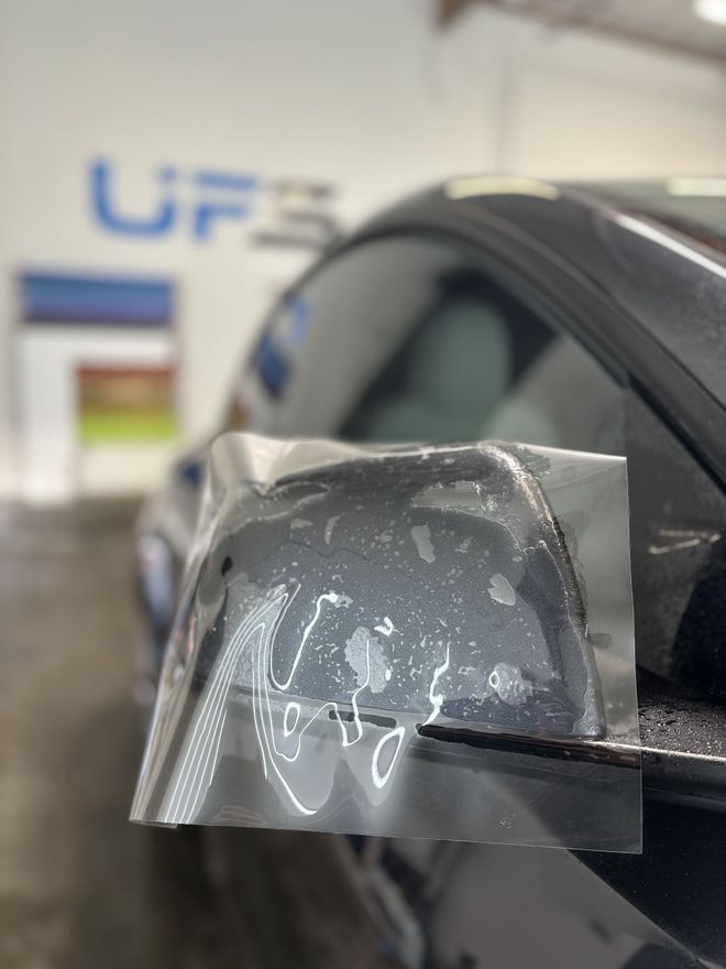 Car wrapped in clear protective film, with a close-up of the side mirror area.