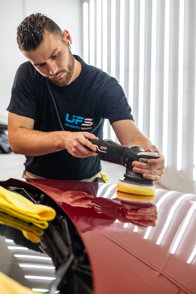 Detailing a red car hood with a polisher in a garage