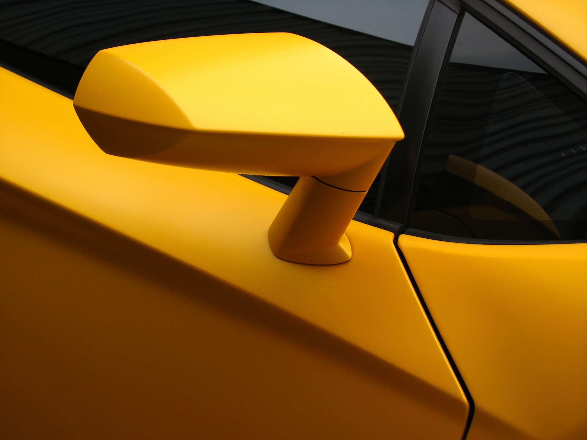 Close-up of a yellow sports car side mirror and door panel.