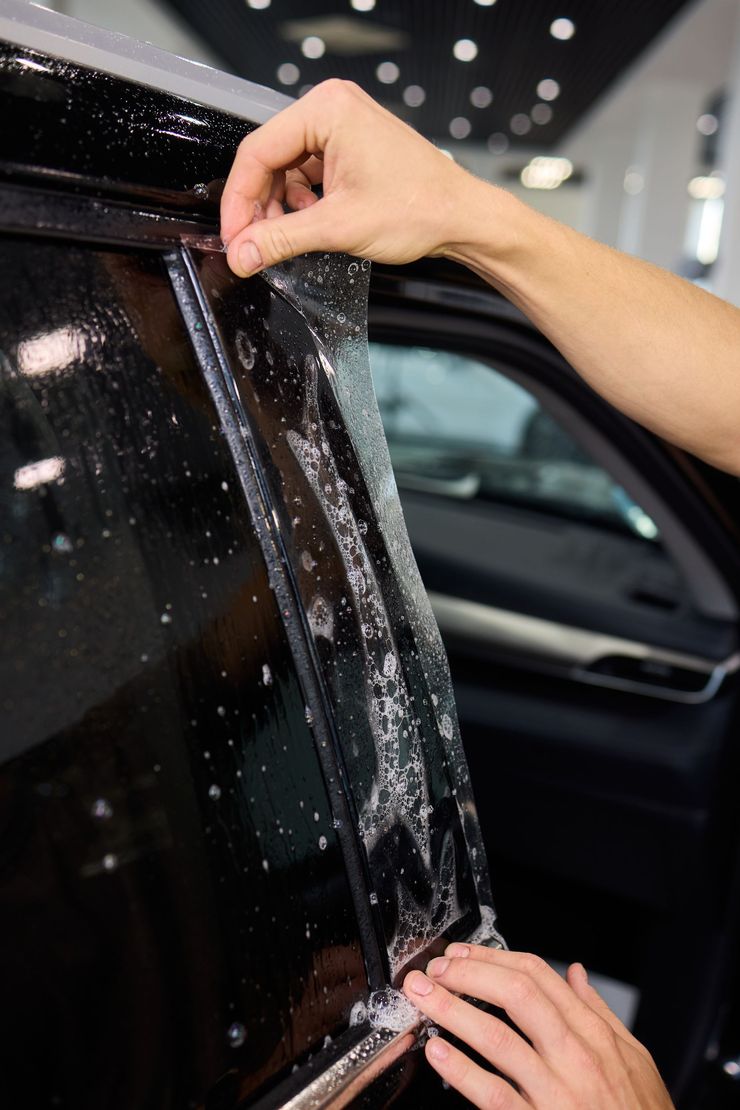 Hands peeling protective film from a car window in an indoor showroom or detailing bay