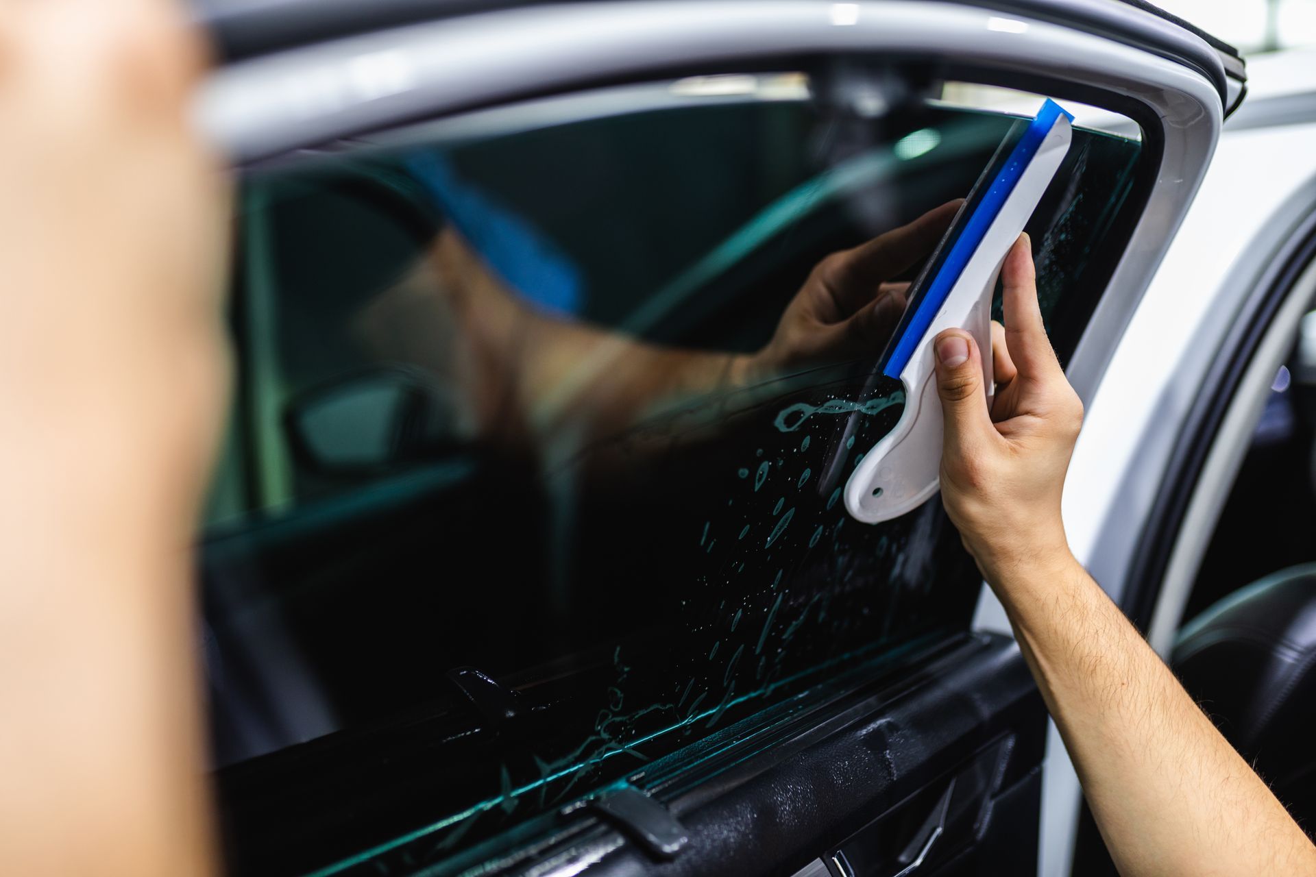 Person using a squeegee to clean a car window with water droplets