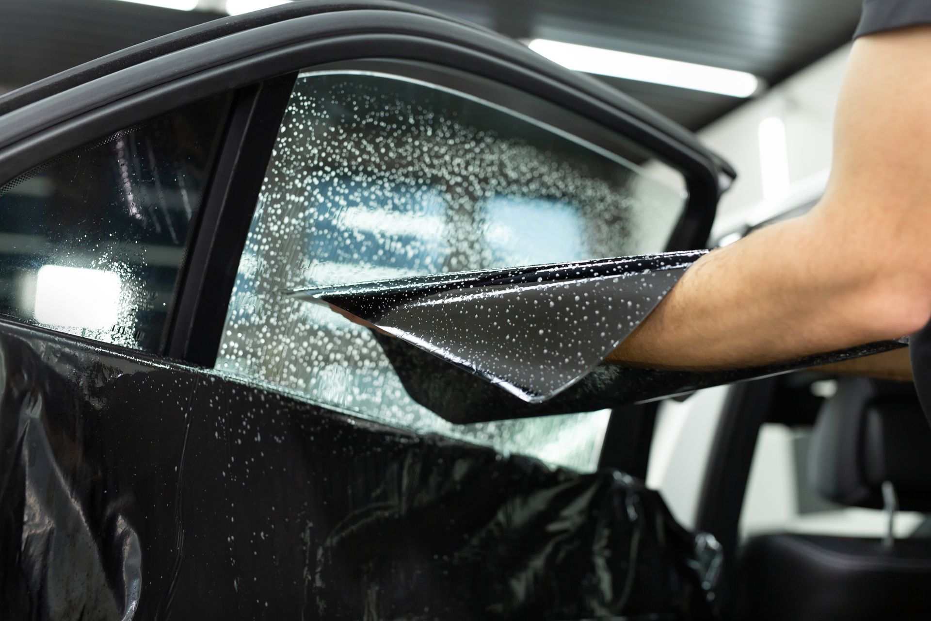 Person cleaning a car window with a squeegee, removing water from cracked glass indoors