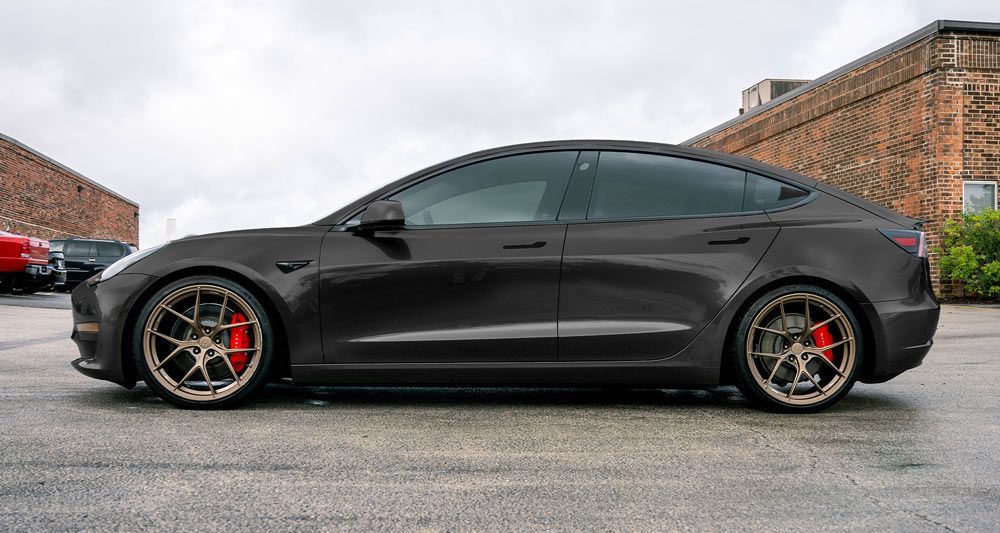 Black lowered sports sedan with red brake calipers, parked in a lot beside brick buildings.