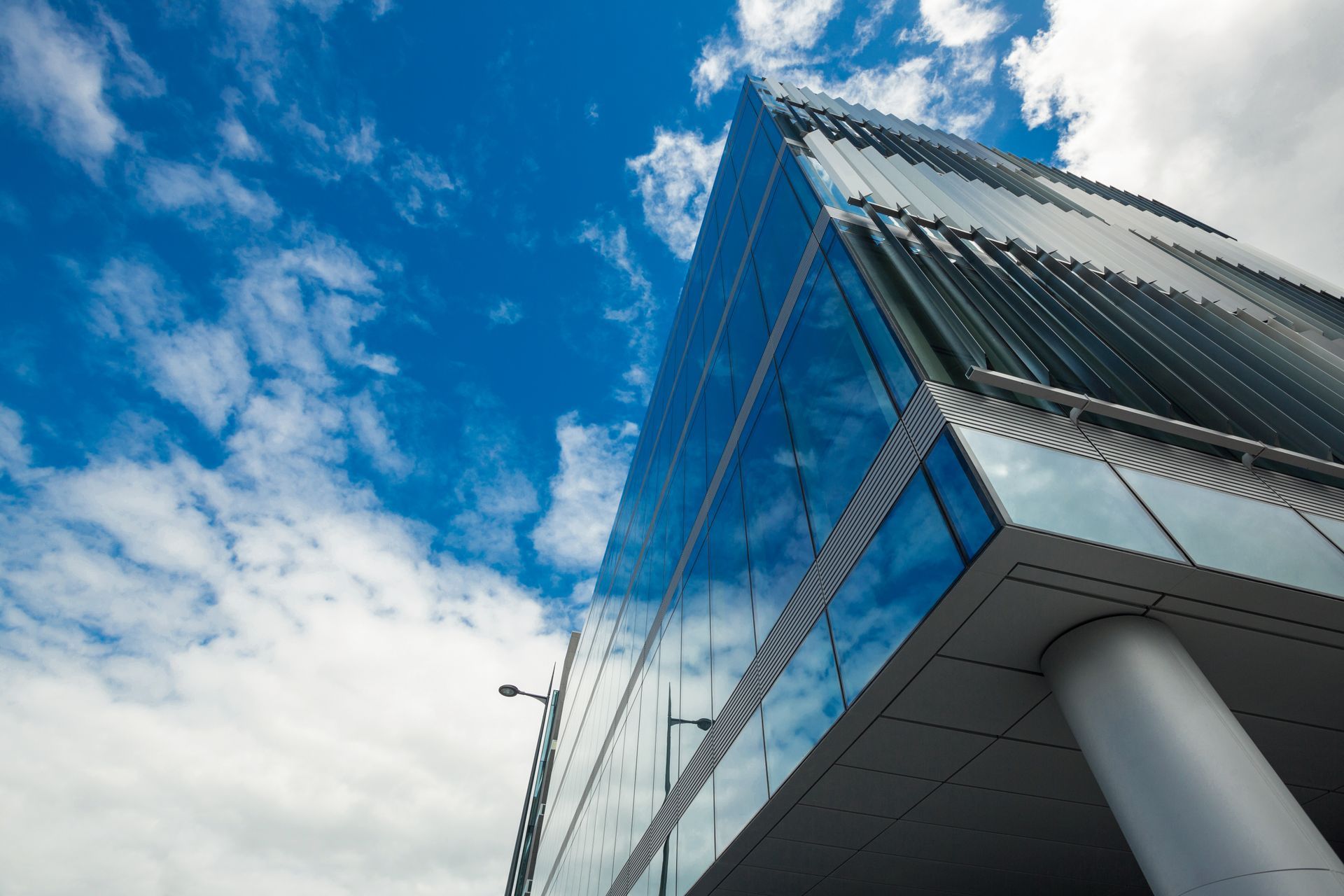Modern glass building against a bright blue sky with clouds
