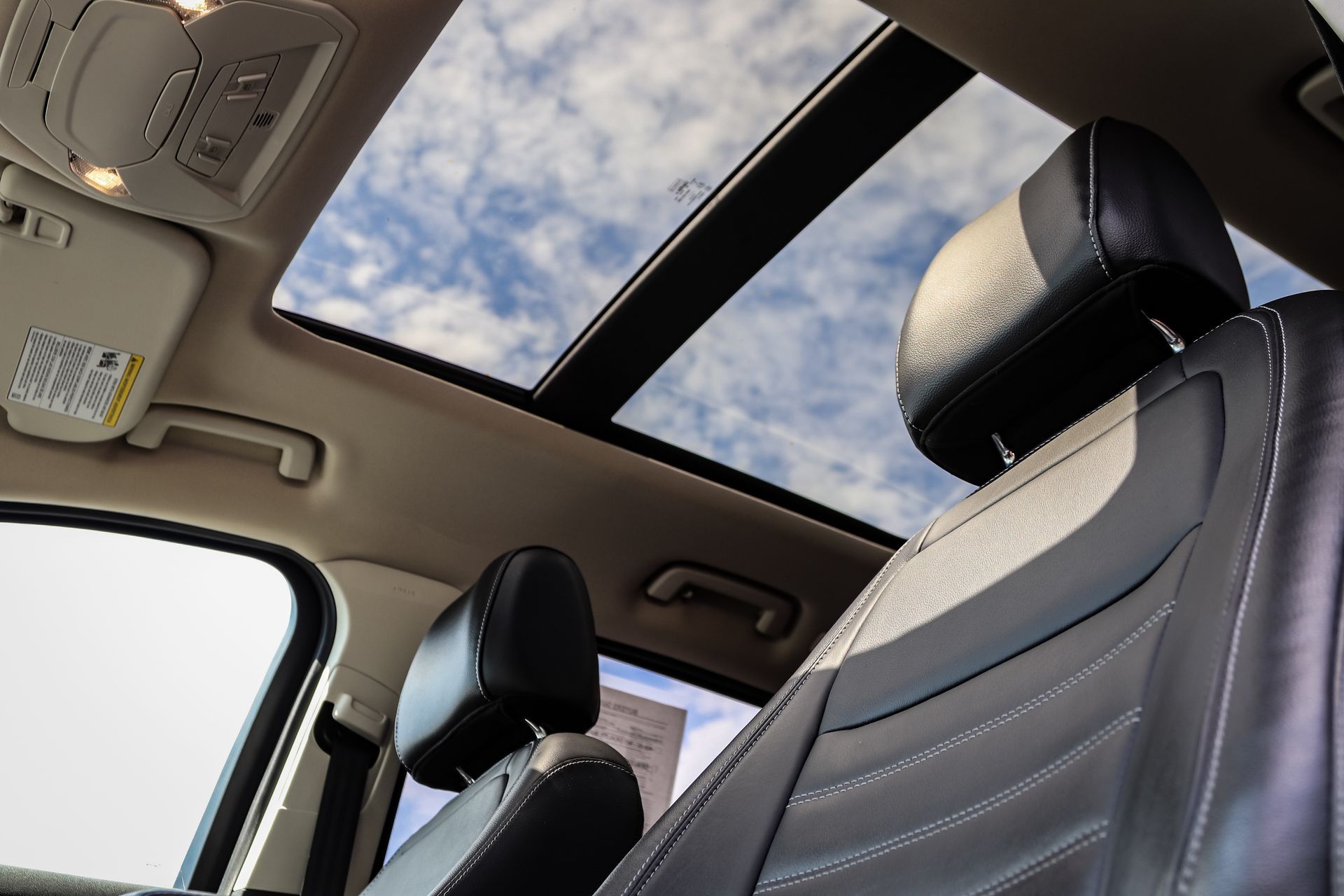 Car interior with black leather seats and a panoramic sunroof showing the sky