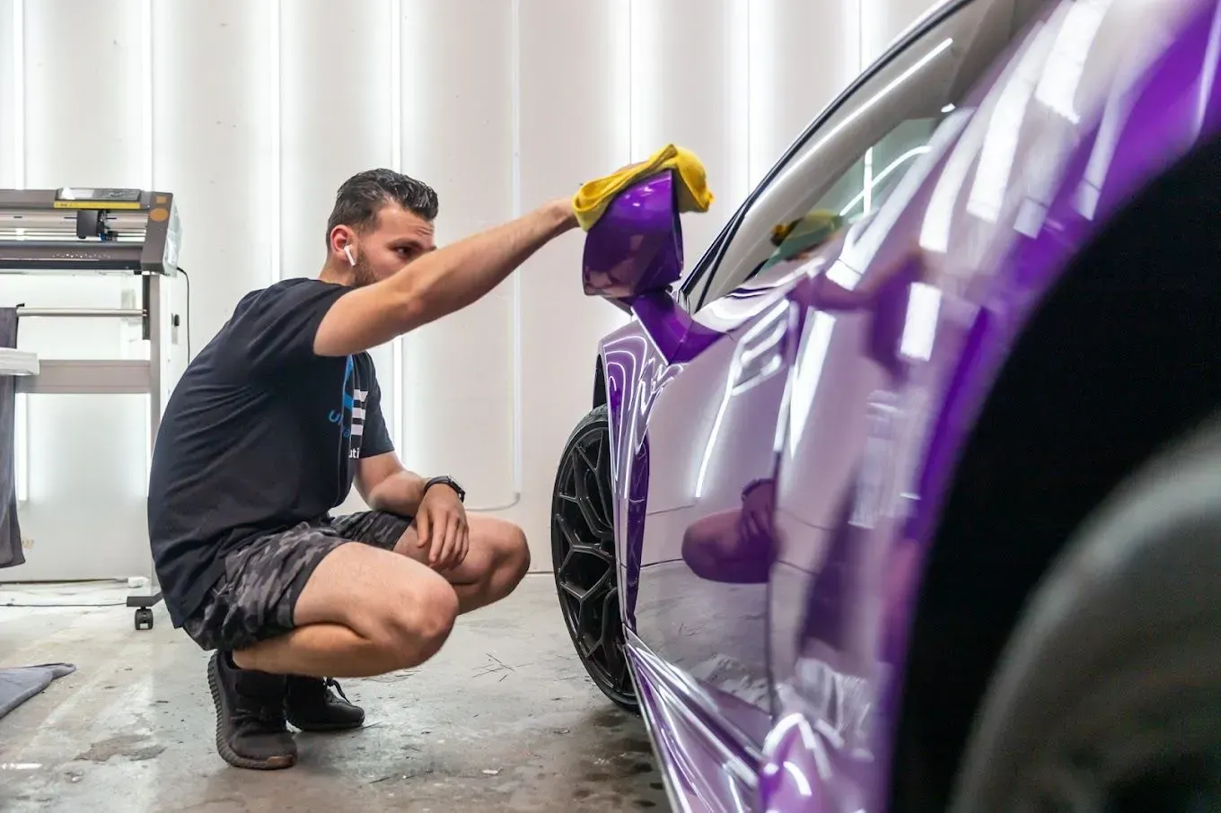Person polishing a purple car in a garage with a yellow cloth
