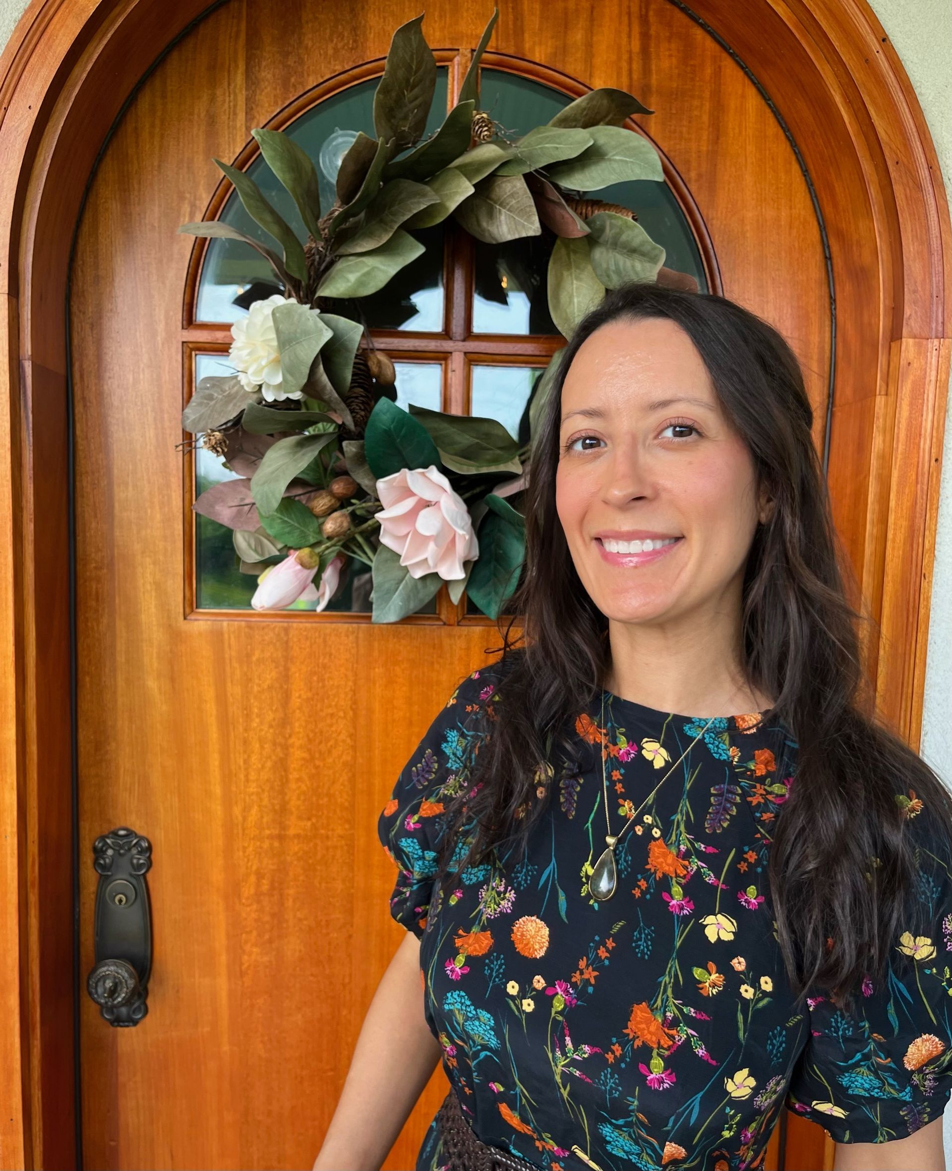 A woman is standing in front of a wooden door with a wreath on it.