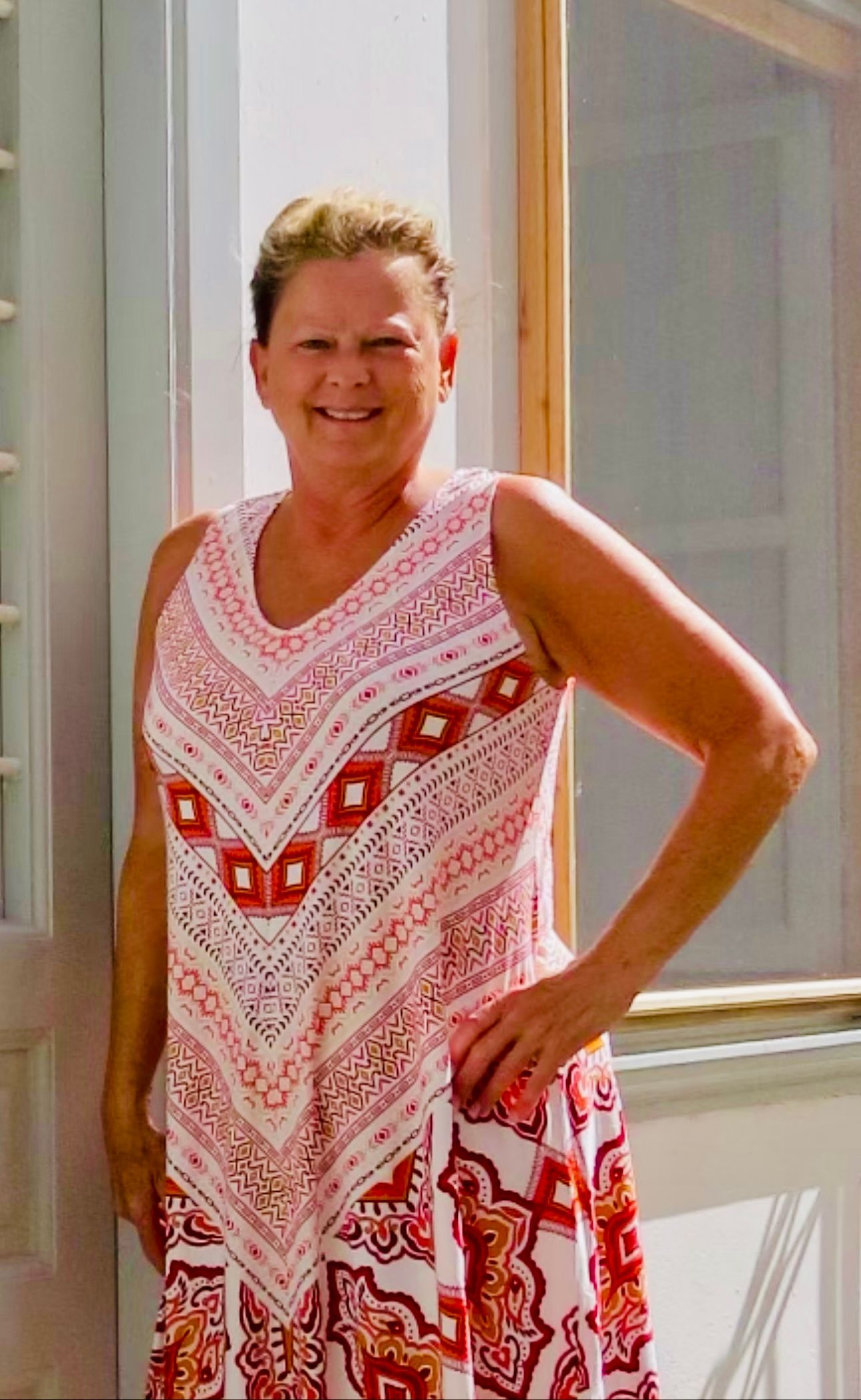A woman in a red and white dress is standing in front of a window.